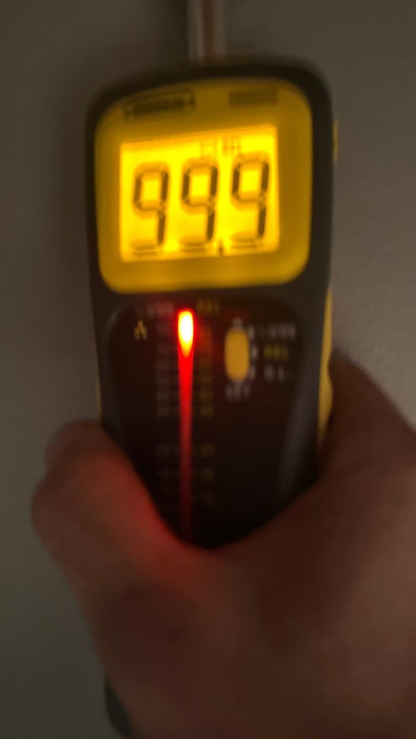 Moisture meter reading saturated drywall beside the bathroom wall cavity